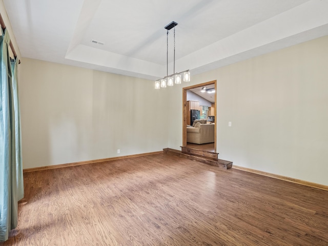 unfurnished room with wood finished floors, a raised ceiling, and baseboards
