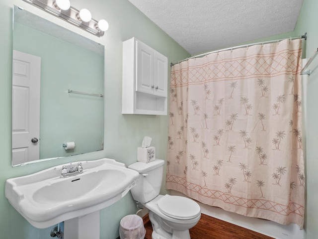 bathroom featuring wood finished floors, a sink, toilet, curtained shower, and a textured ceiling