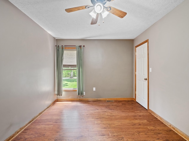 empty room with a textured ceiling, wood finished floors, a ceiling fan, and baseboards