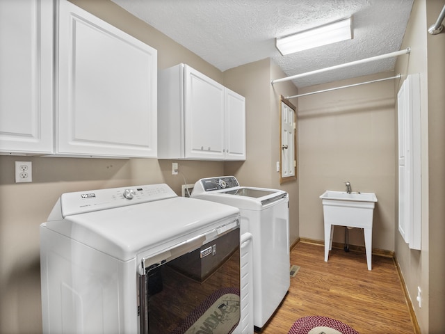 washroom with washer and dryer, cabinet space, light wood finished floors, a textured ceiling, and baseboards