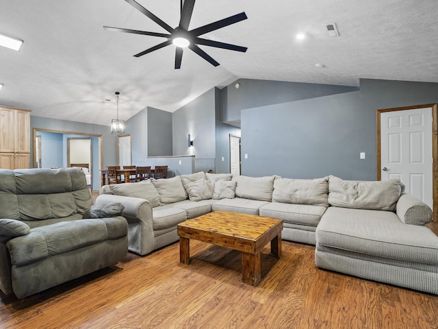 living room with ceiling fan, vaulted ceiling, light wood finished floors, and a chandelier