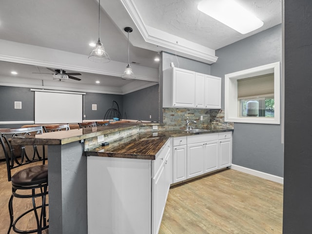 kitchen with a kitchen breakfast bar, white cabinets, decorative backsplash, a sink, and light wood-style flooring