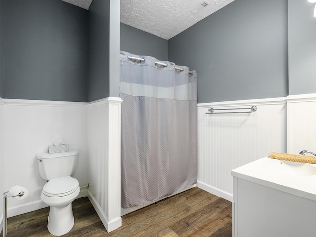 bathroom featuring wood finished floors, a wainscoted wall, toilet, a textured ceiling, and a shower with shower curtain