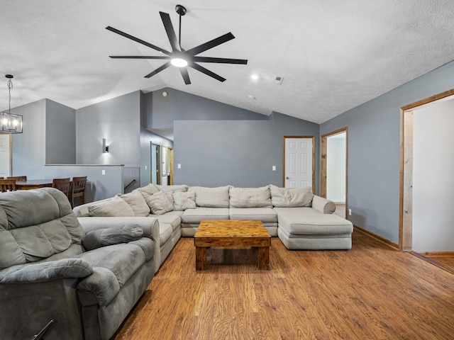 living room featuring vaulted ceiling, wood finished floors, a chandelier, ceiling fan, and baseboards