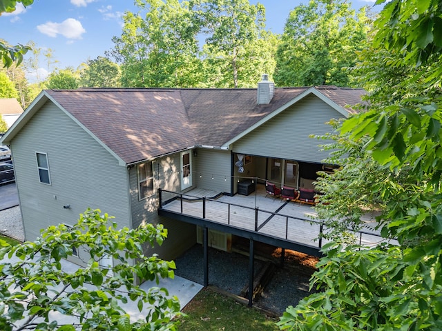 rear view of property with roof with shingles, a chimney, and a wooden deck