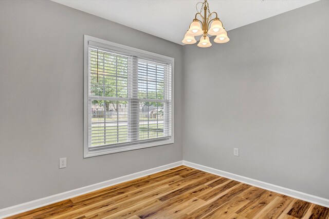 spare room with a chandelier, baseboards, and light wood-style floors