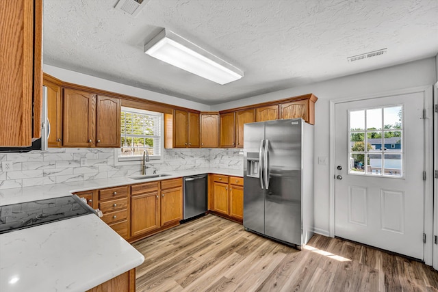 kitchen with stainless steel appliances, a sink, brown cabinetry, a textured ceiling, and light wood-type flooring