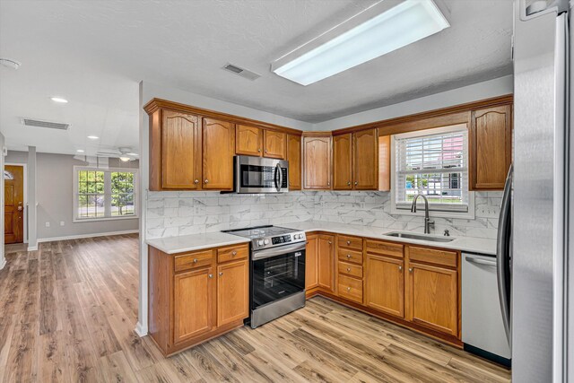 kitchen featuring appliances with stainless steel finishes, a sink, light wood-type flooring, light countertops, and brown cabinets