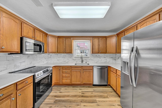kitchen featuring appliances with stainless steel finishes, a sink, light wood-type flooring, and brown cabinets