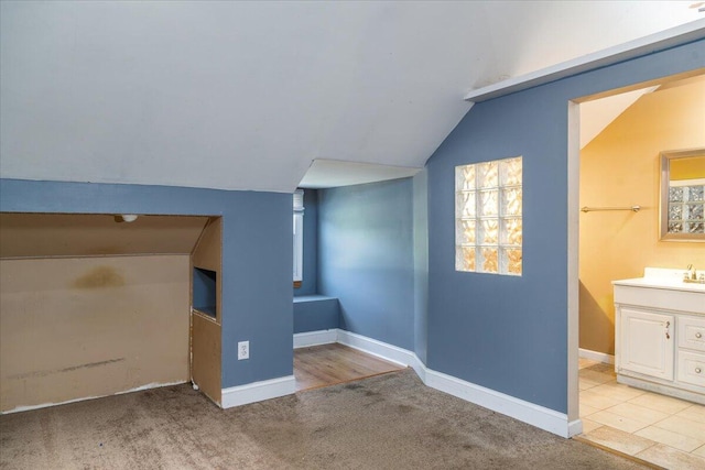 additional living space with vaulted ceiling, baseboards, carpet floors, a sink, and plenty of natural light
