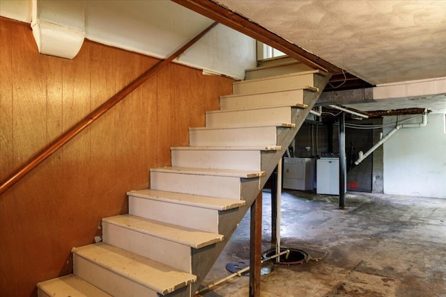 stairway with washer / dryer, unfinished concrete flooring, and wooden walls