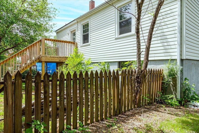 view of side of home featuring fence, a deck, a chimney, and stairs