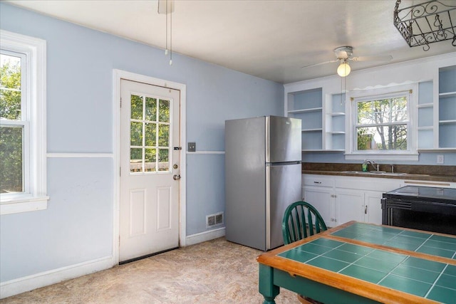 kitchen featuring freestanding refrigerator, a sink, open shelves, and plenty of natural light