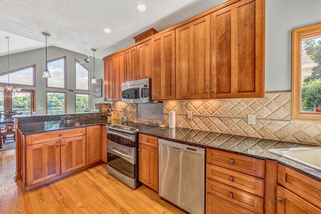 kitchen with stainless steel appliances, lofted ceiling, a peninsula, light wood-type flooring, and brown cabinets