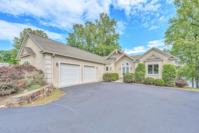 view of front of property featuring an attached garage, driveway, stucco siding, and roof with shingles