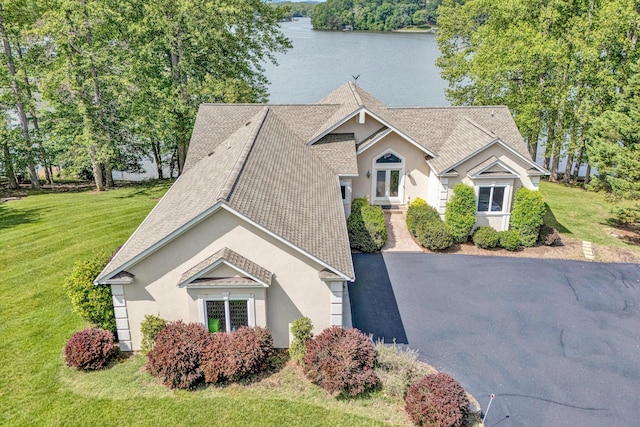 view of front of home featuring roof with shingles, stucco siding, a front yard, and a water view