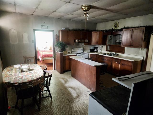 kitchen with electric stove, a drop ceiling, a sink, ceiling fan, and a kitchen island