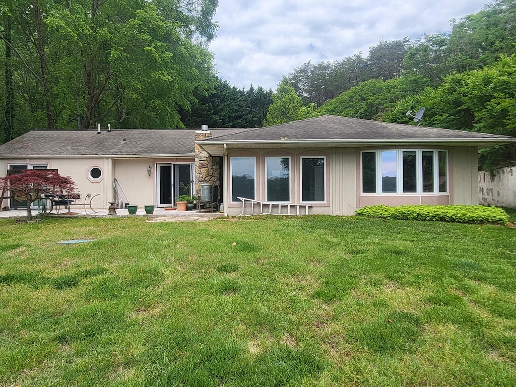 back of house featuring a lawn, a patio area, and roof with shingles