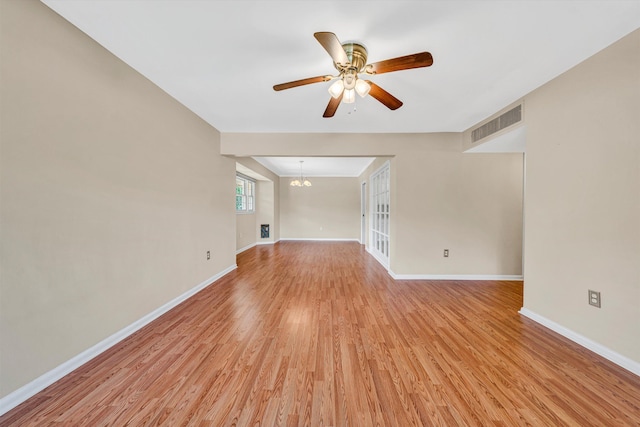 spare room featuring a ceiling fan, light wood-style flooring, baseboards, and a chandelier