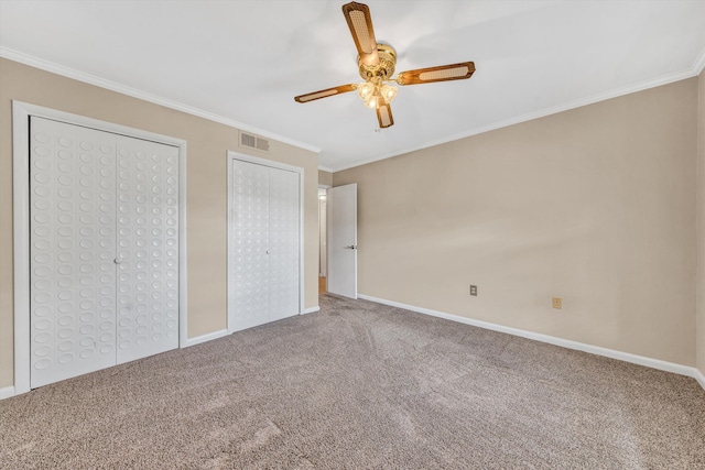 unfurnished bedroom with carpet flooring, ornamental molding, two closets, baseboards, and ceiling fan