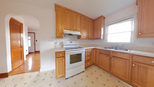 kitchen with electric range, a sink, under cabinet range hood, arched walkways, and light floors