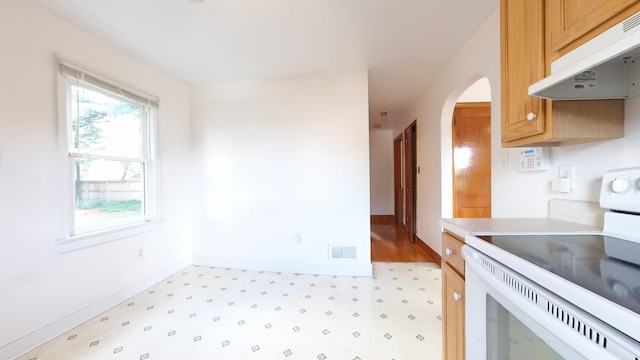 kitchen featuring white range with electric cooktop, under cabinet range hood, light floors, arched walkways, and baseboards
