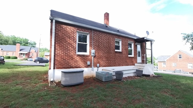 back of property featuring brick siding, a yard, a chimney, and central air condition unit