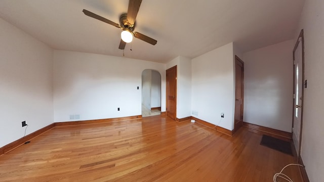 empty room featuring ceiling fan, light wood-style flooring, arched walkways, and baseboards