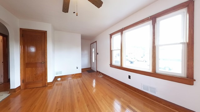 spare room with light wood-style flooring, arched walkways, a ceiling fan, and baseboards