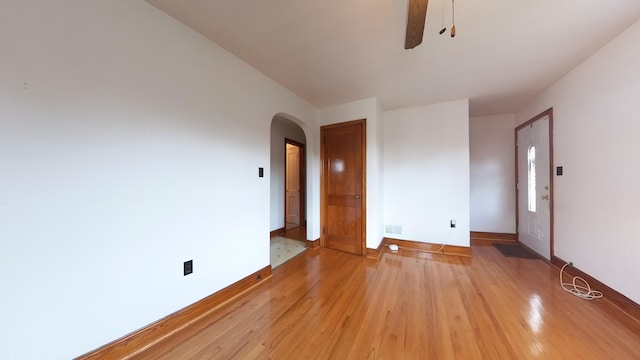 spare room with ceiling fan, light wood-style floors, arched walkways, and baseboards
