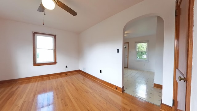 empty room featuring arched walkways, ceiling fan, light wood finished floors, and baseboards