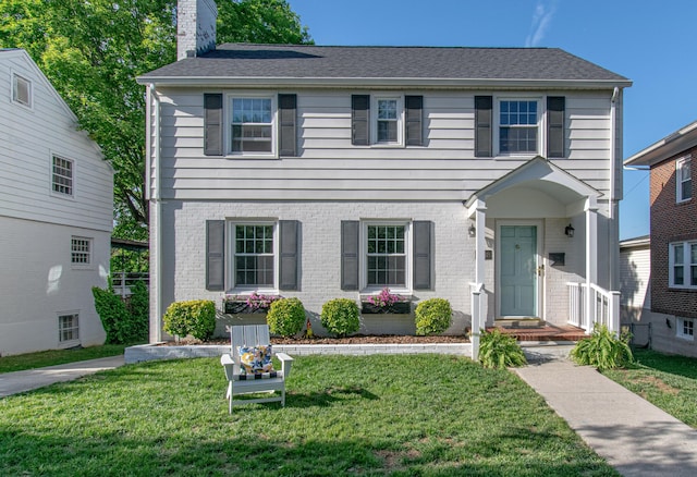 view of front of house featuring a chimney, a front yard, and brick siding