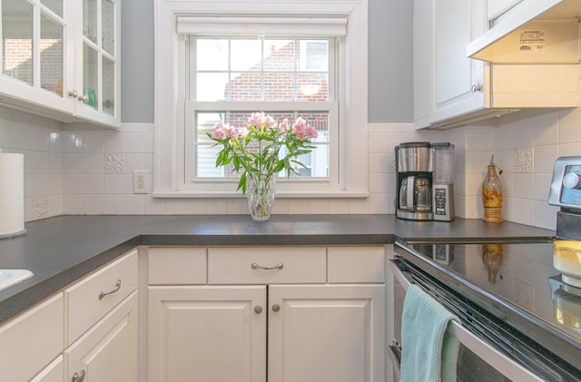 kitchen featuring electric stove, under cabinet range hood, dark countertops, white cabinetry, and glass insert cabinets