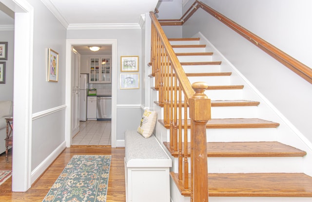 stairs featuring wood finished floors, ornamental molding, and baseboards