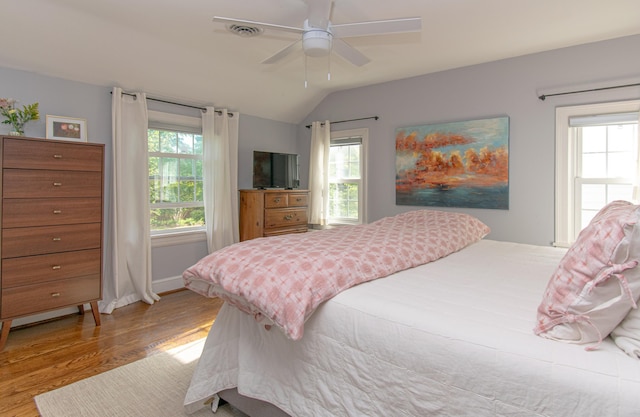 bedroom with wood finished floors, vaulted ceiling, multiple windows, a ceiling fan, and baseboards