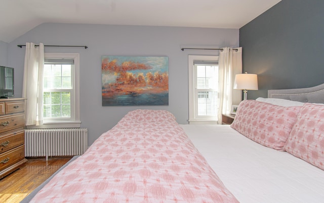 bedroom with radiator heating unit, lofted ceiling, and wood finished floors