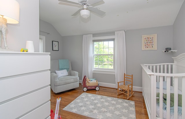 bedroom with a crib, wood finished floors, vaulted ceiling, baseboards, and ceiling fan
