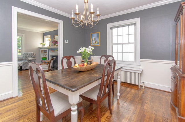 dining space featuring radiator heating unit, a chandelier, wood finished floors, crown molding, and a fireplace