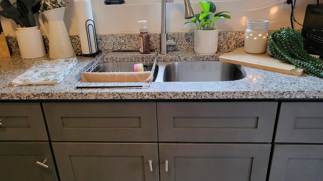 kitchen view of gray cabinetry, a sink, and light stone counters
