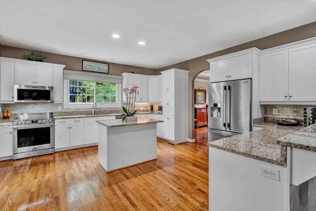 kitchen featuring appliances with stainless steel finishes, a sink, decorative backsplash, arched walkways, and white cabinets
