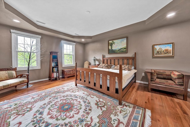 bedroom with wood finished floors, baseboards, recessed lighting, and a raised ceiling