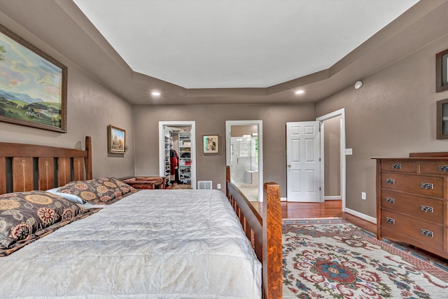 bedroom with a spacious closet, wood finished floors, a tray ceiling, a closet, and ensuite bath