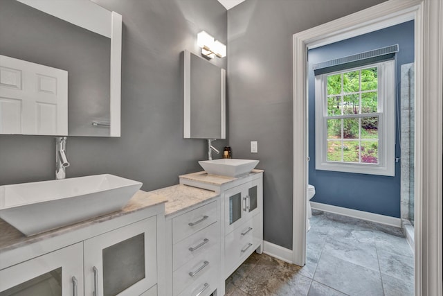 full bath with baseboards, double vanity, toilet, and stone finish flooring