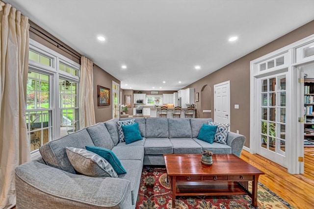 living room with recessed lighting, light wood-style flooring, arched walkways, and baseboards
