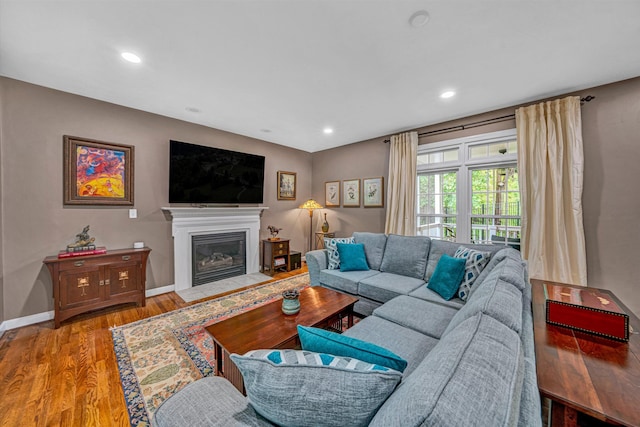 living area featuring a fireplace with flush hearth, wood finished floors, baseboards, and recessed lighting