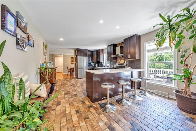 414 Mallard Cove Rd, Moneta, VA 24121 - kitchen featuring stainless steel fridge, wall chimney exhaust hood, dark brown cabinetry, a peninsula, and brick patterned floors
