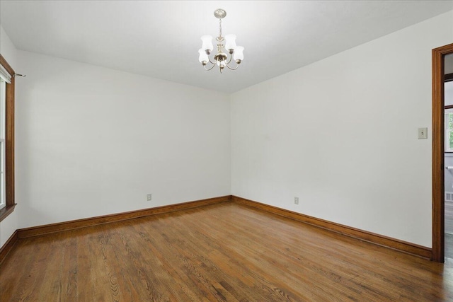 unfurnished room featuring a chandelier, wood finished floors, and baseboards