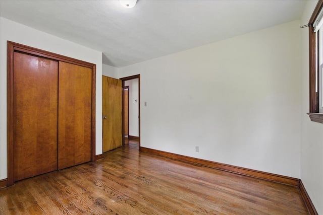 unfurnished bedroom with wood finished floors, baseboards, and a closet