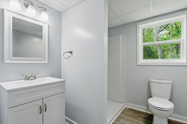 bathroom with a drop ceiling, toilet, vanity, wood finished floors, and baseboards