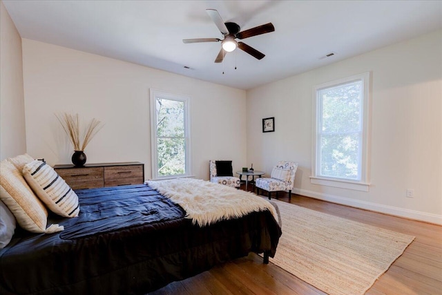 bedroom with multiple windows, wood finished floors, baseboards, and a ceiling fan